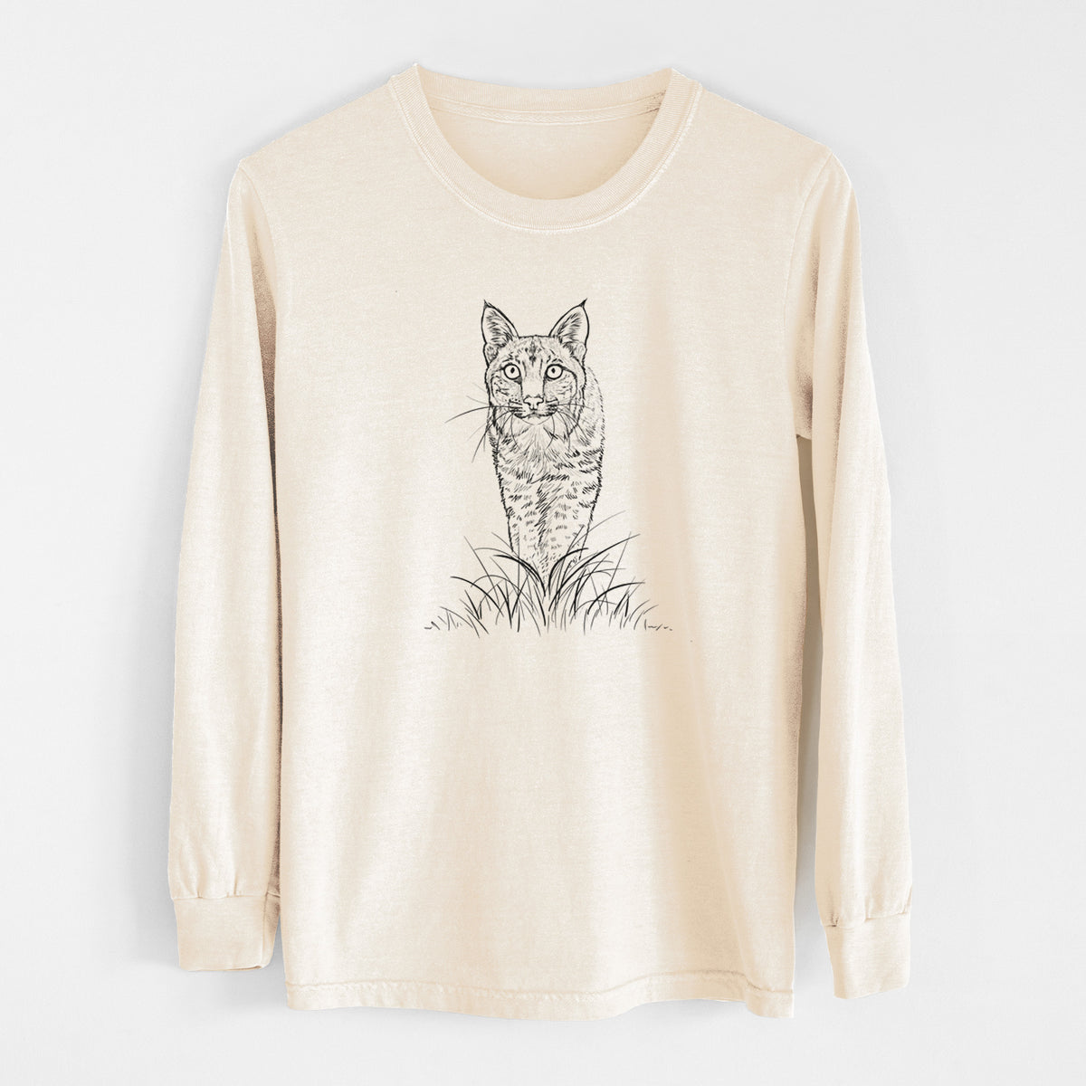 Ivory Comfort Colors long sleeve shirt laid flat, printed with a black ink illustration of a bobcat standing in tall grass, facing forward.