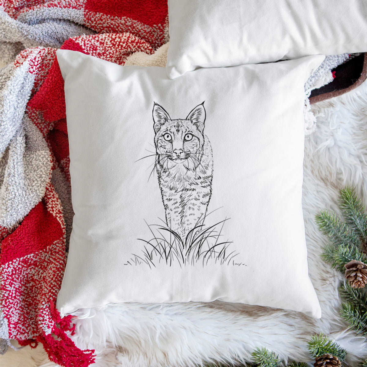 White pillow cover printed with a black ink illustration of a bobcat standing in tall grass, facing forward, on a woven chair.