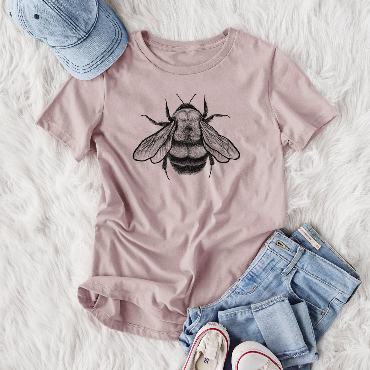 Women's relaxed fit cotton t-shirt printed with a detailed black ink illustration of a rusty patched bumble bee with its wings spread, seen from above, styled flat on a white faux fur rug with jeans.