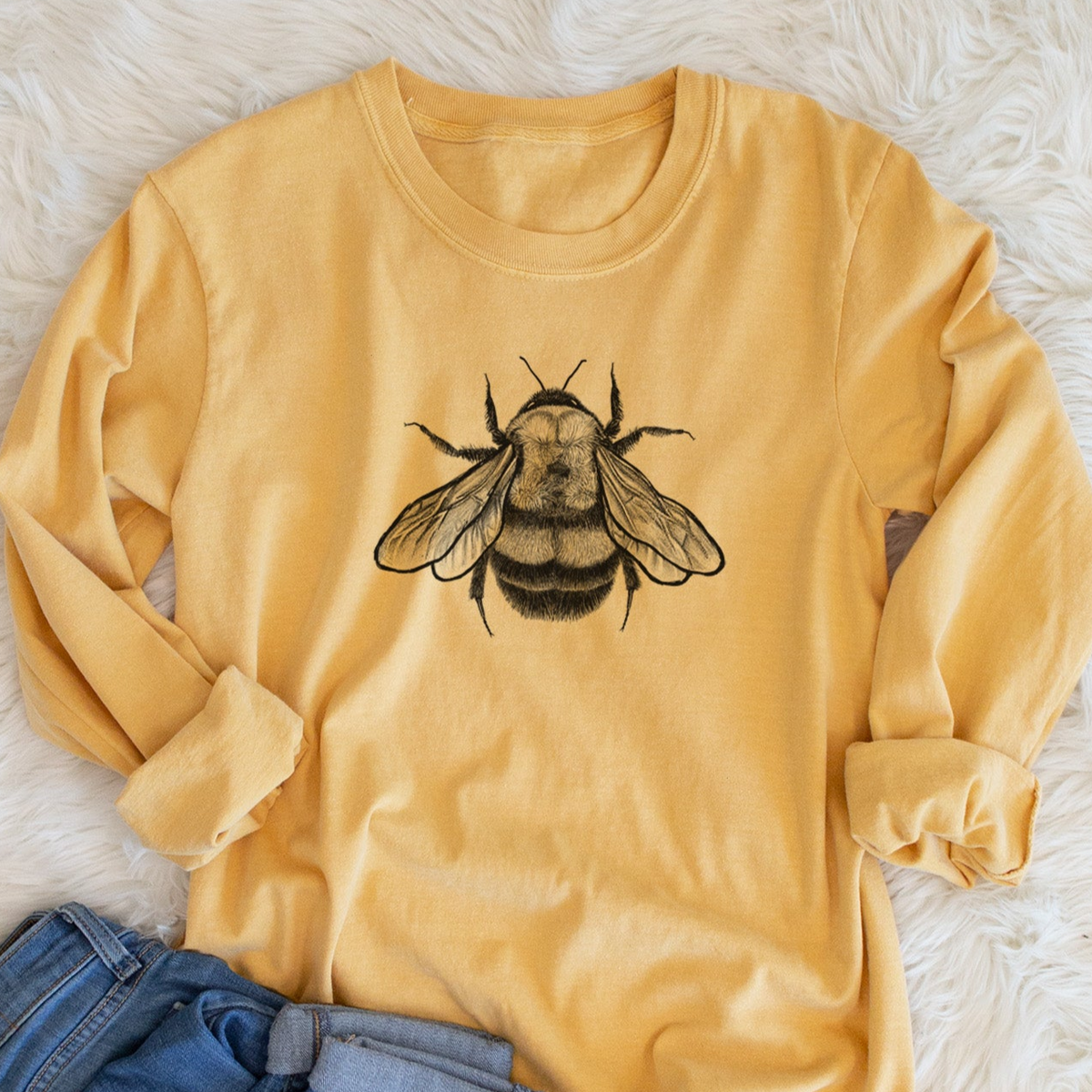 Golden wheat yellow Comfort Colors long sleeve shirt printed with a detailed black ink illustration of a rusty patched bumble bee with its wings spread, seen from above, shown in a lifestyle photo.