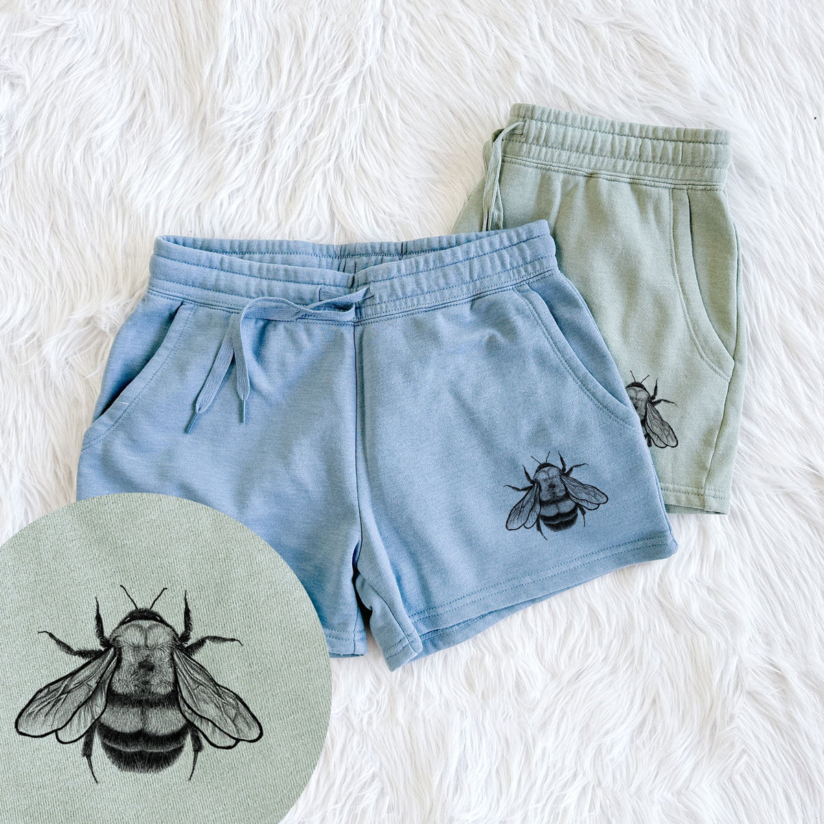 Two pairs of Cali Wave shorts in different colors printed with a detailed black ink illustration of a rusty patched bumble bee with its wings spread, seen from above, with a close-up of the print.