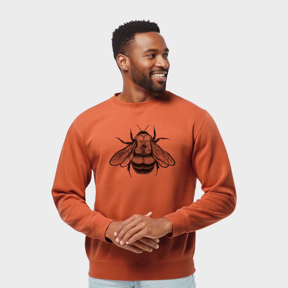 Model wearing an amber orange pigment dyed crewneck sweatshirt printed with a detailed black ink illustration of a rusty patched bumble bee with its wings spread, seen from above.