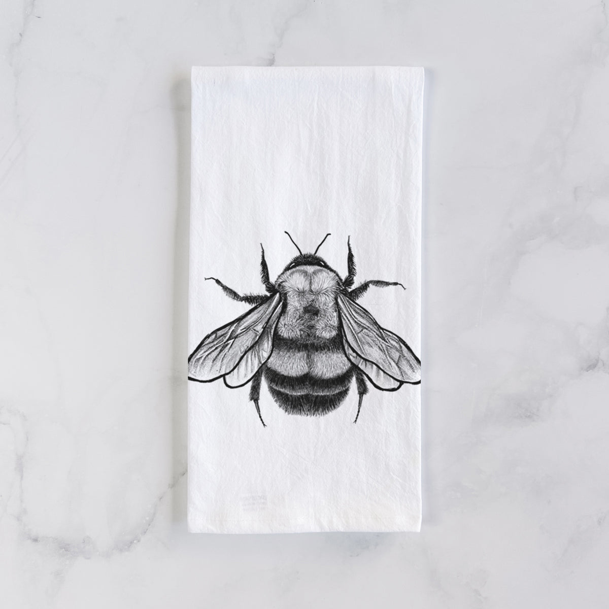 White cotton tea towel laid flat on marble, printed with a detailed black ink illustration of a rusty patched bumble bee with its wings spread, seen from above.