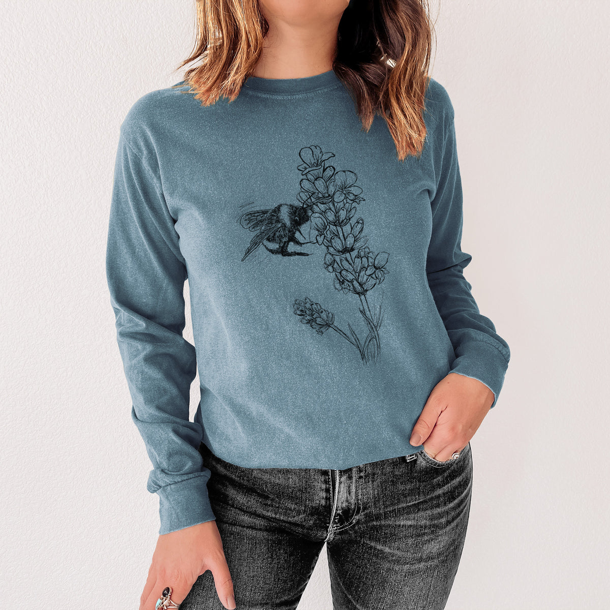 Steel blue Comfort Colors long sleeve shirt printed with a black ink illustration of a bumble bee visiting a sprig of lavender, shown in a lifestyle photo.