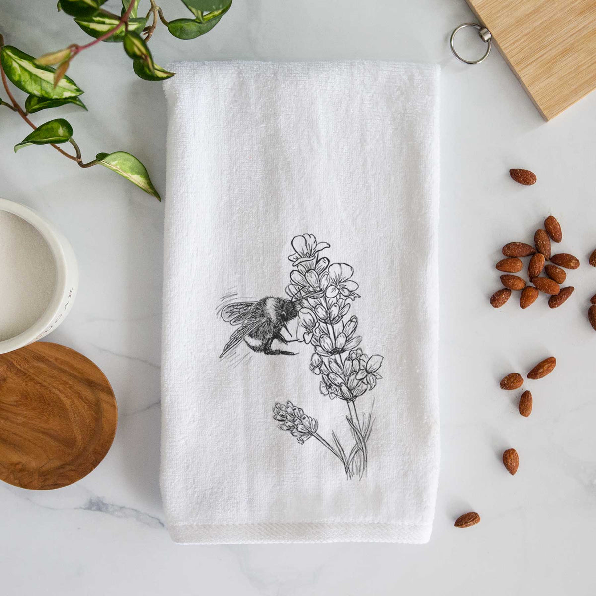 White hand towel printed with a black ink illustration of a bumble bee visiting a sprig of lavender.