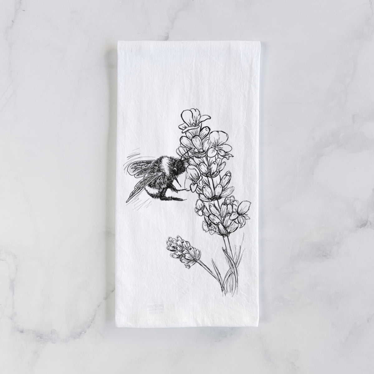 White cotton tea towel laid flat on marble, printed with a black ink illustration of a bumble bee visiting a sprig of lavender.