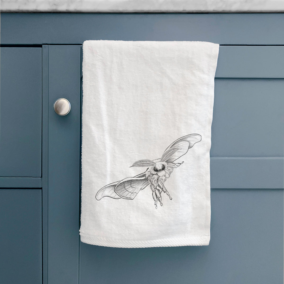 White hand towel printed with a black ink illustration of a silk moth with its wings spread, hanging on a cabinet door.