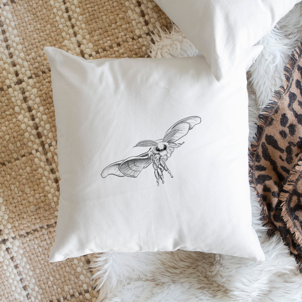White pillow cover printed with a black ink illustration of a silk moth with its wings spread, on a woven chair.