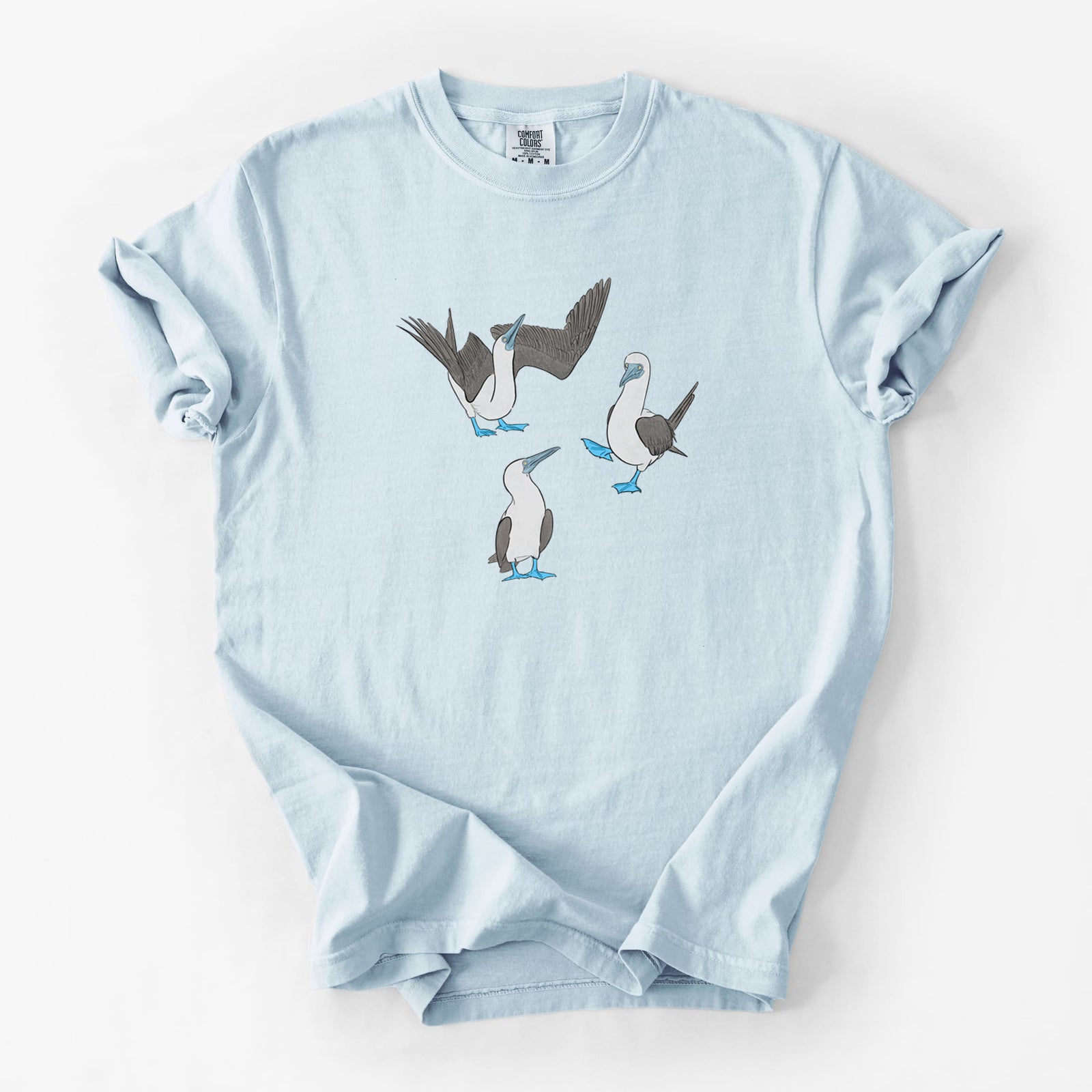 Chambray blue Comfort Colors t-shirt laid flat, printed with a full-color illustration of three blue-footed boobies, one with its wings spread.
