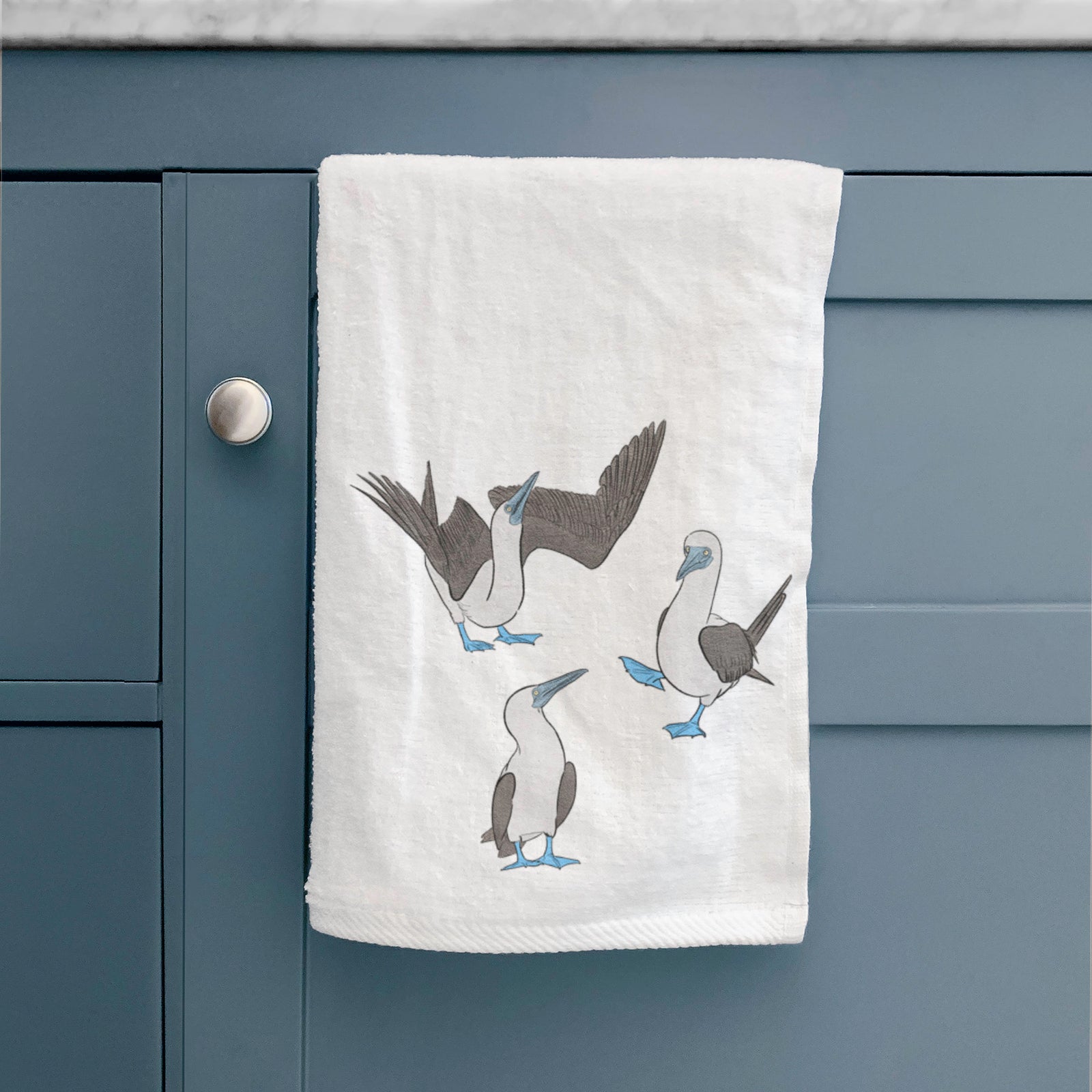 White hand towel printed with a full-color illustration of three blue-footed boobies, one with its wings spread.