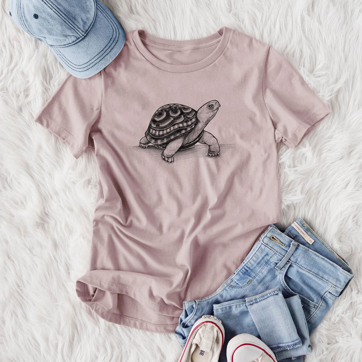 Women's relaxed fit cotton t-shirt printed with a detailed black ink illustration of an eastern box turtle walking, styled flat on a white faux fur rug with jeans.