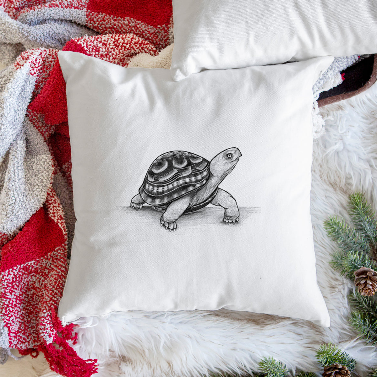 White pillow cover printed with a detailed black ink illustration of an eastern box turtle walking, on a woven chair.