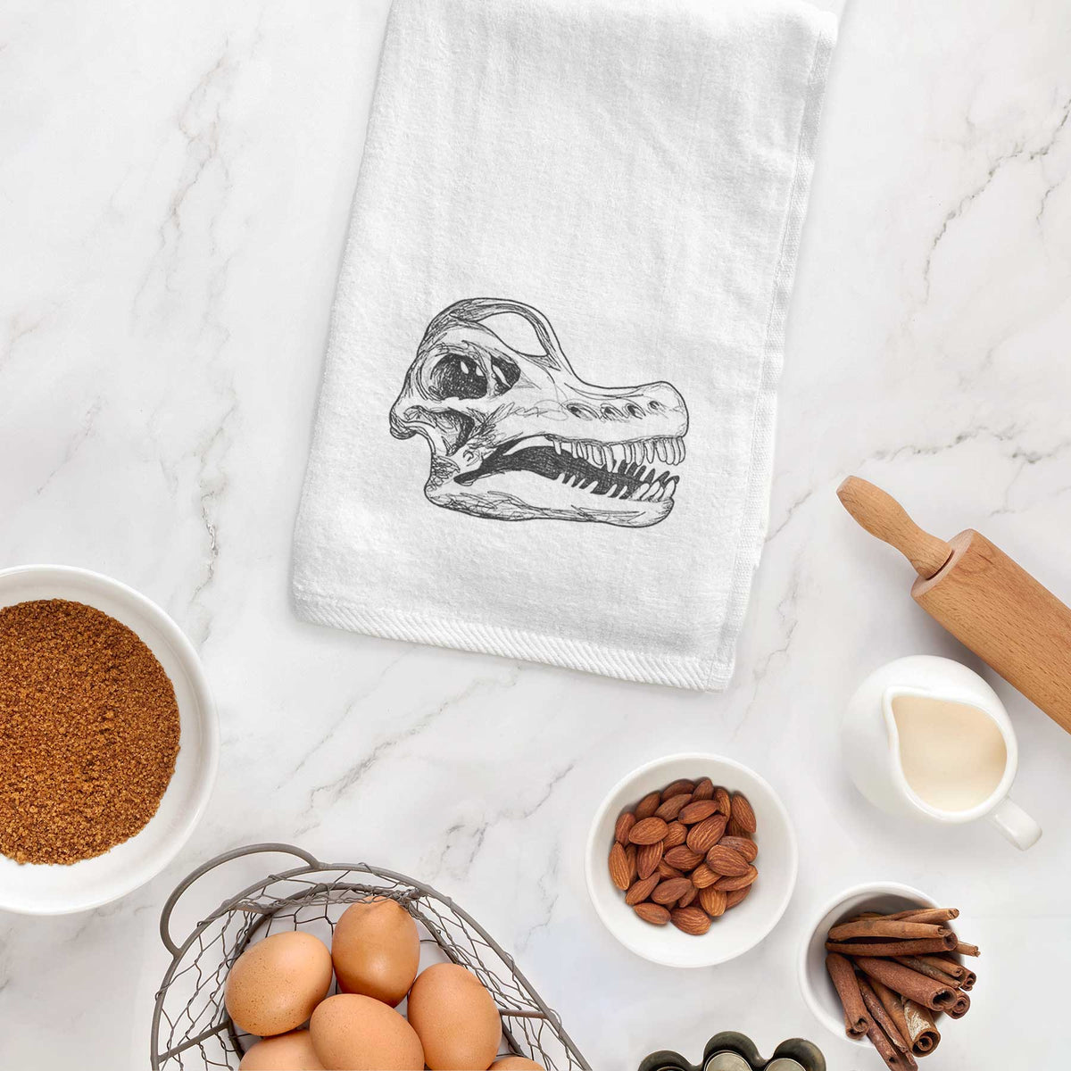 White hand towel printed with a detailed black ink illustration of a Brachiosaurus skull, hanging on a cabinet door.