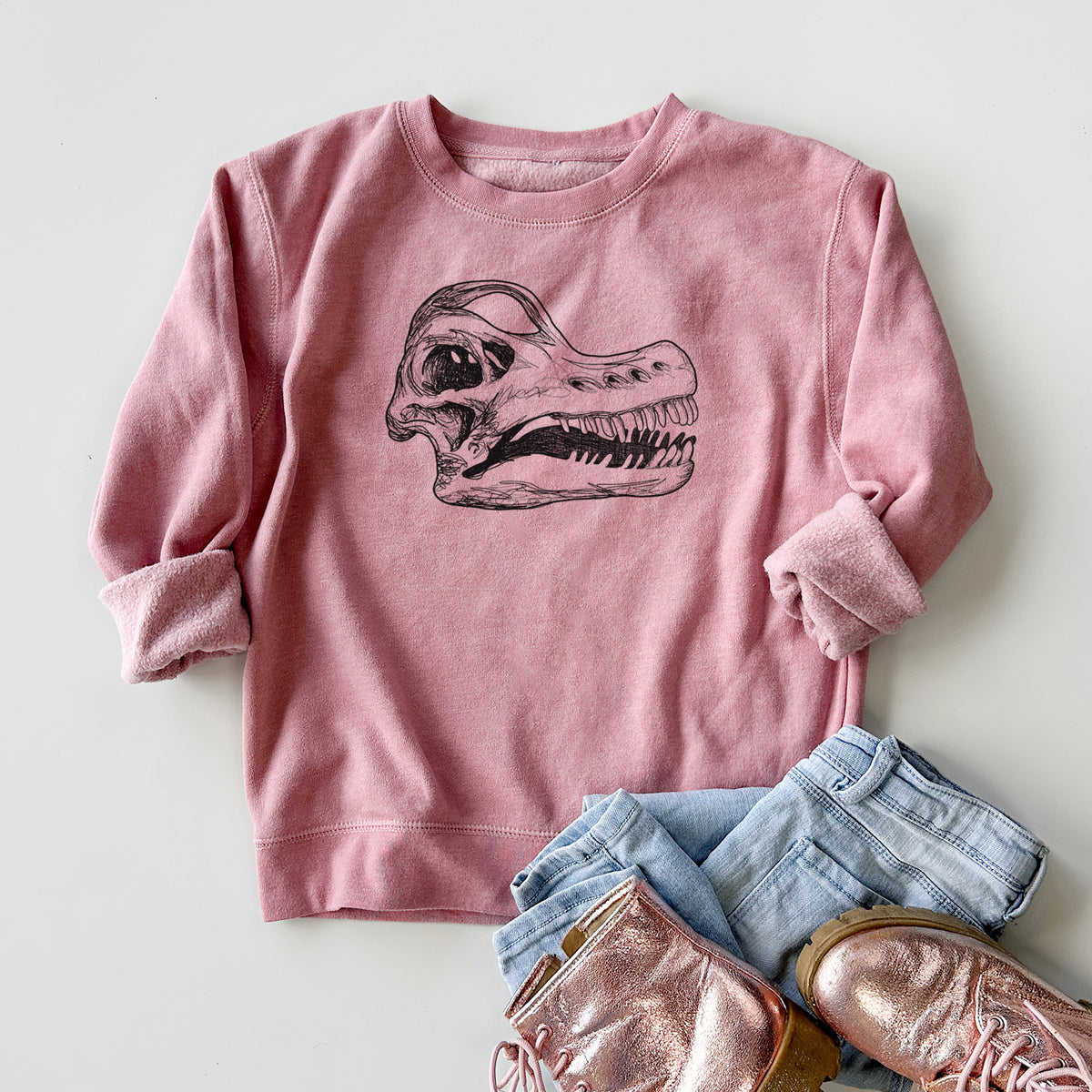 Youth crewneck sweatshirt printed with a detailed black ink illustration of a Brachiosaurus skull, styled flat with jeans and boots.