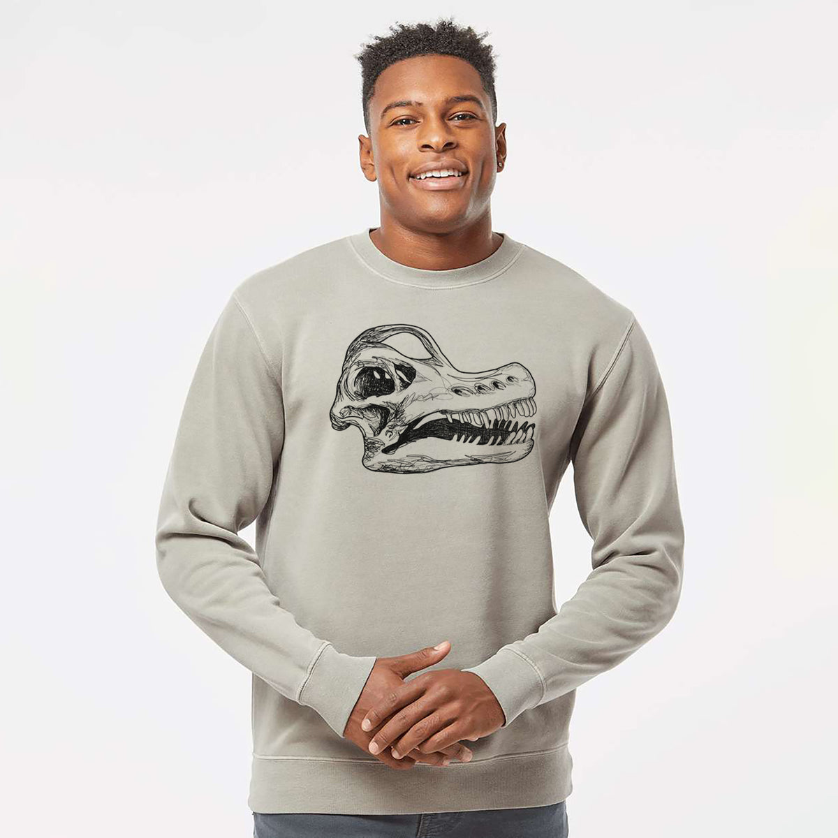 Model wearing a cement grey pigment dyed crewneck sweatshirt printed with a detailed black ink illustration of a Brachiosaurus skull.