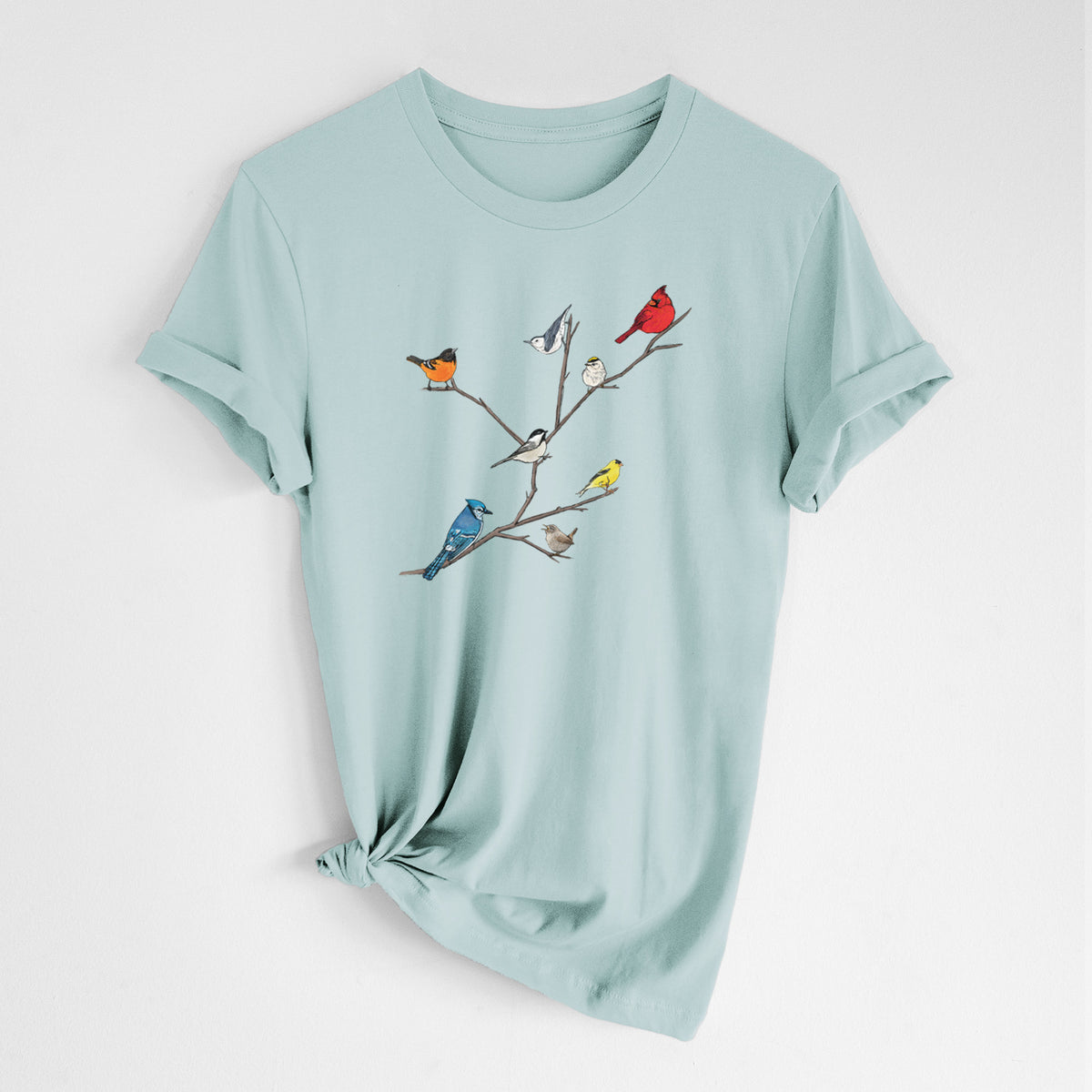 Dusty blue lightweight cotton t-shirt laid flat with the sleeves rolled, printed with a full-color illustration of backyard birds, including a cardinal, blue jay, goldfinch and robin, perched on bare branches.