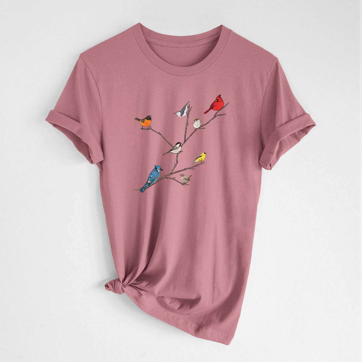 Mauve pink lightweight cotton t-shirt laid flat with the sleeves rolled, printed with a full-color illustration of backyard birds, including a cardinal, blue jay, goldfinch and robin, perched on bare branches.