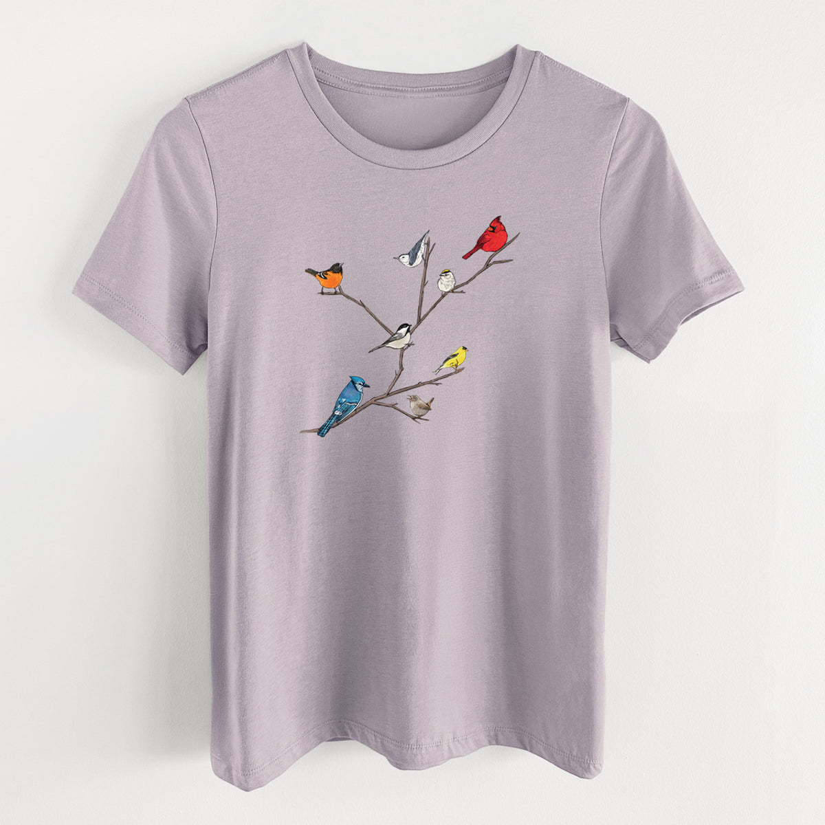 Light violet women's relaxed fit cotton t-shirt laid flat, printed with a full-color illustration of backyard birds, including a cardinal, blue jay, goldfinch and robin, perched on bare branches.