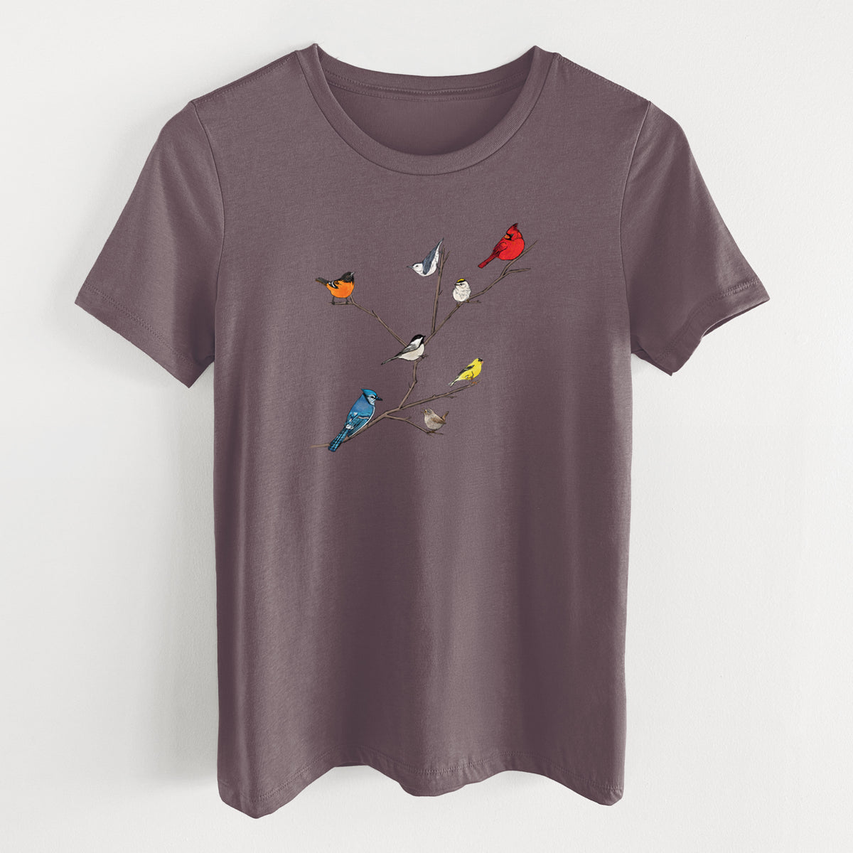 Purple storm women's relaxed fit cotton t-shirt laid flat, printed with a full-color illustration of backyard birds, including a cardinal, blue jay, goldfinch and robin, perched on bare branches.