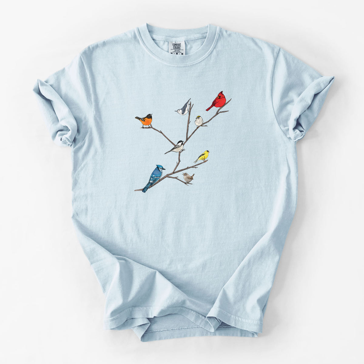 Chambray blue Comfort Colors t-shirt laid flat, printed with a full-color illustration of backyard birds, including a cardinal, blue jay, goldfinch and robin, perched on bare branches.