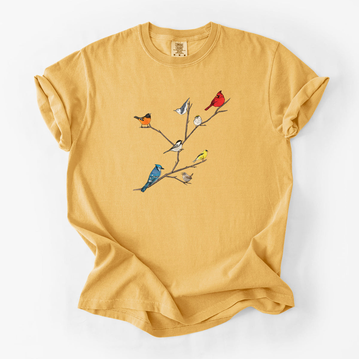 Golden wheat yellow Comfort Colors t-shirt laid flat, printed with a full-color illustration of backyard birds, including a cardinal, blue jay, goldfinch and robin, perched on bare branches.