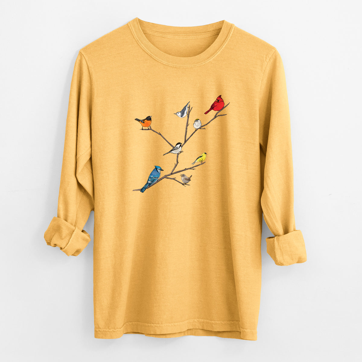 Golden wheat yellow Comfort Colors long sleeve shirt laid flat with the cuffs rolled, printed with a full-color illustration of backyard birds, including a cardinal, blue jay, goldfinch and robin, perched on bare branches.