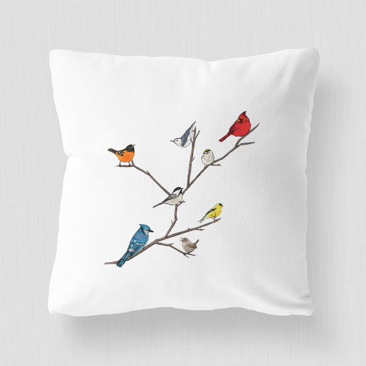 White pillow cover printed with a full-color illustration of backyard birds, including a cardinal, blue jay, goldfinch and robin, perched on bare branches.