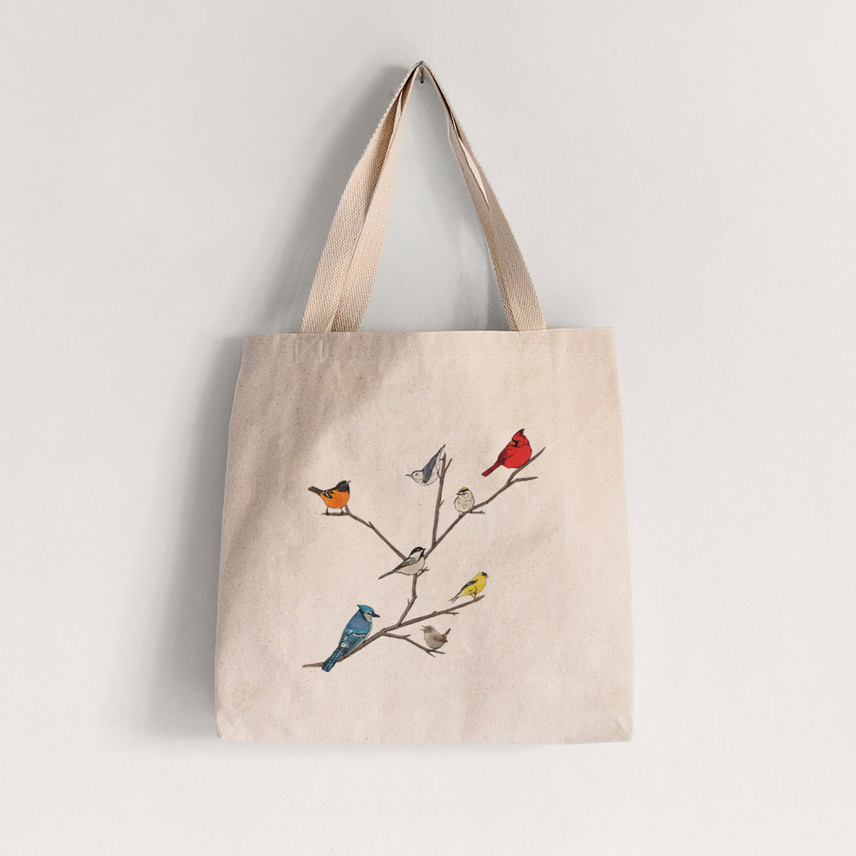 Natural canvas tote bag printed with a full-color illustration of backyard birds, including a cardinal, blue jay, goldfinch and robin, perched on bare branches.