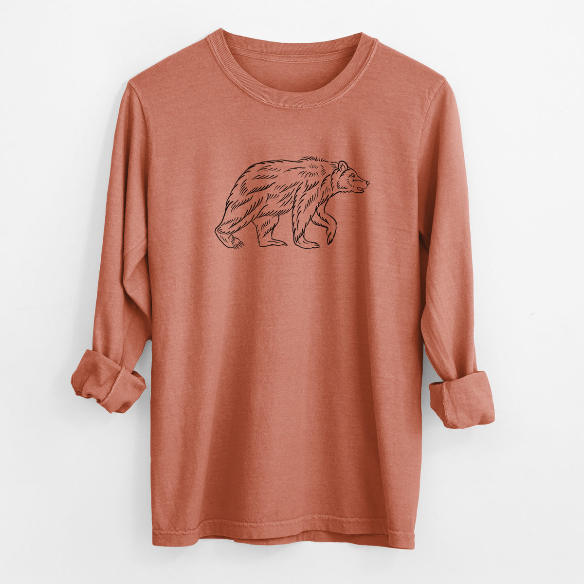 Yam burnt orange Comfort Colors long sleeve shirt laid flat with the cuffs rolled, printed with a black ink illustration of a brown bear walking.