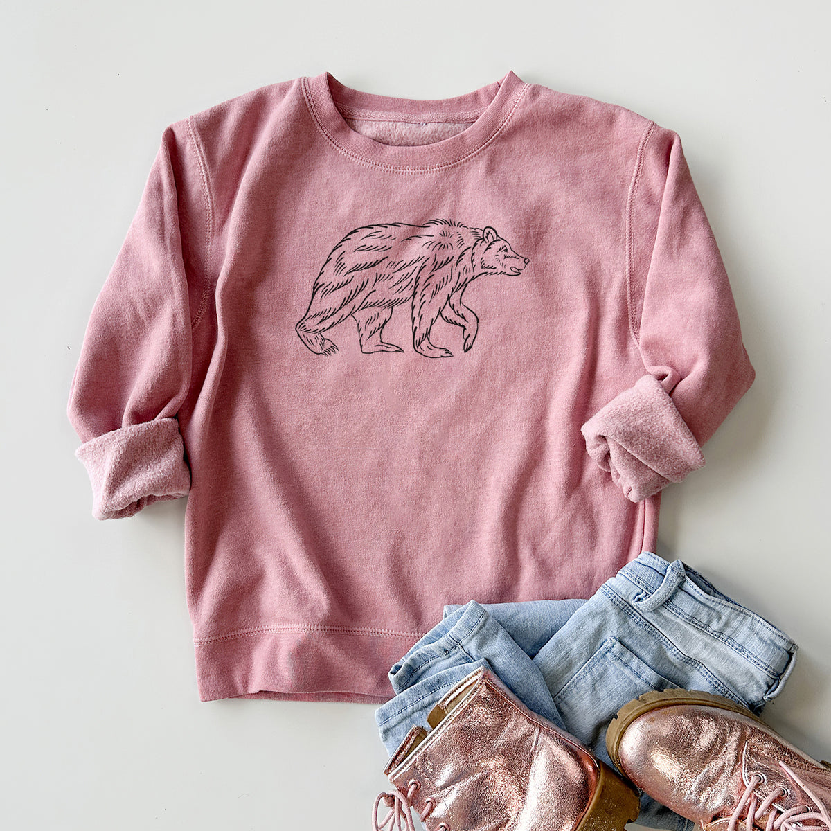 Youth crewneck sweatshirt printed with a black ink illustration of a brown bear walking, styled flat with jeans and boots.