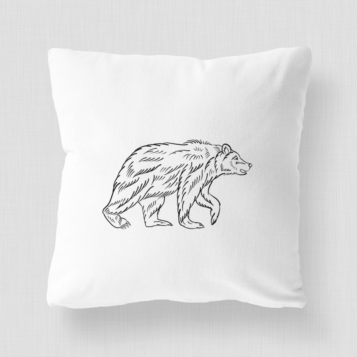 White pillow cover printed with a black ink illustration of a brown bear walking.