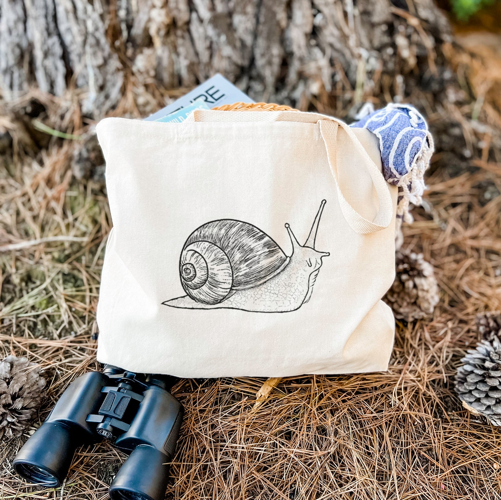 Natural canvas tote bag printed with a detailed black ink illustration of a brown garden snail with its spiral shell.