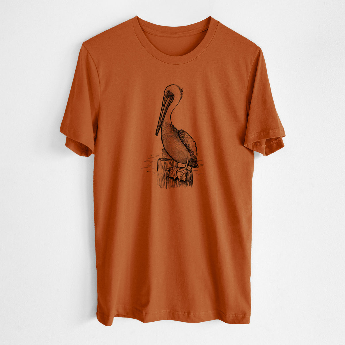 Autumn lightweight cotton t-shirt laid flat, printed with a detailed black ink illustration of a brown pelican perched on a wooden piling.