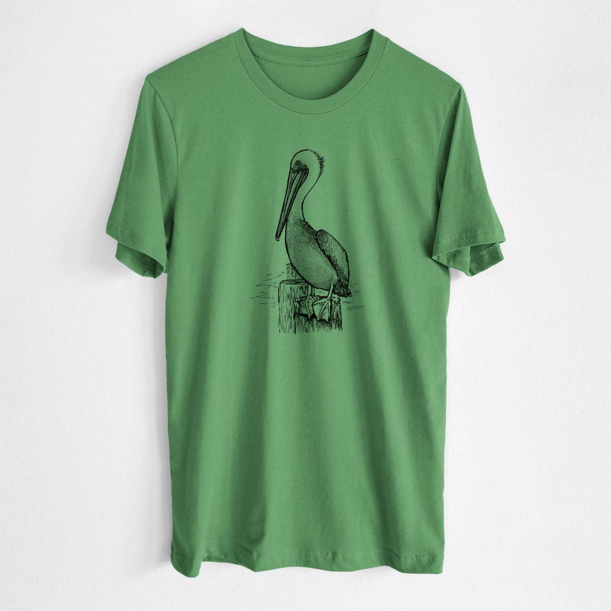 Leaf green lightweight cotton t-shirt laid flat, printed with a detailed black ink illustration of a brown pelican perched on a wooden piling.