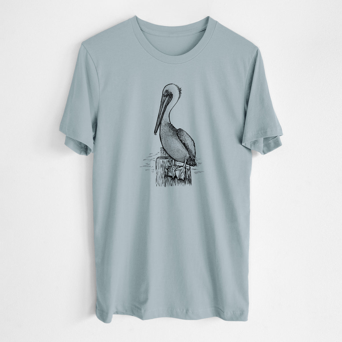 Vintage denim lightweight cotton t-shirt laid flat, printed with a detailed black ink illustration of a brown pelican perched on a wooden piling.