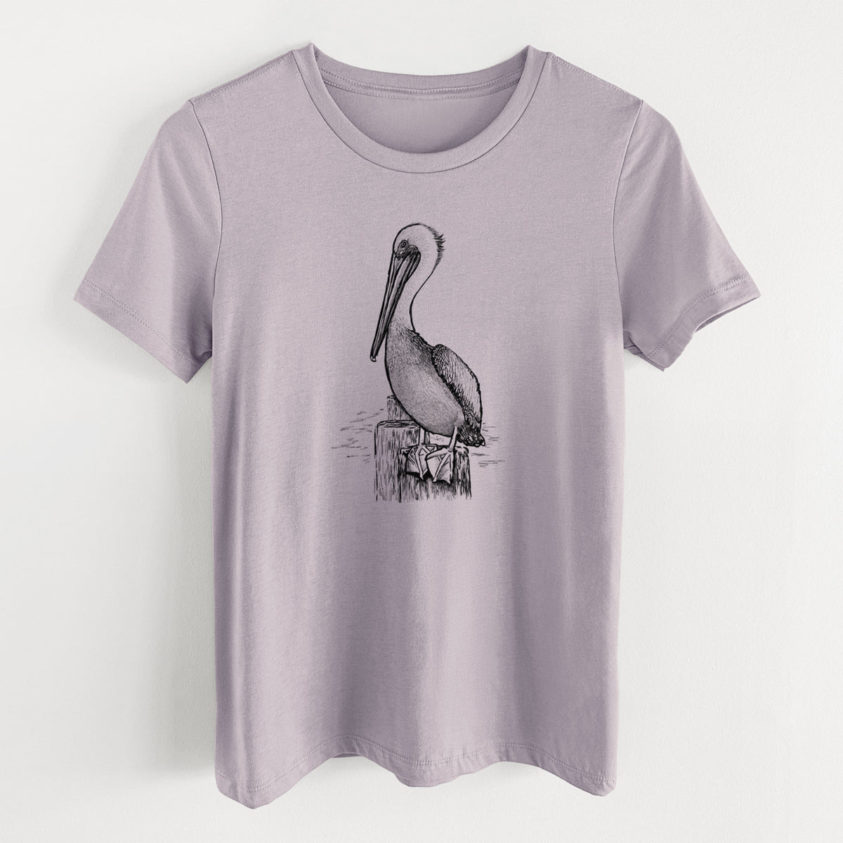 Light violet women's relaxed fit cotton t-shirt laid flat, printed with a detailed black ink illustration of a brown pelican perched on a wooden piling.