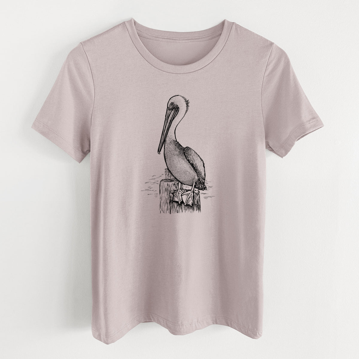 Pink gravel women's relaxed fit cotton t-shirt laid flat, printed with a detailed black ink illustration of a brown pelican perched on a wooden piling.
