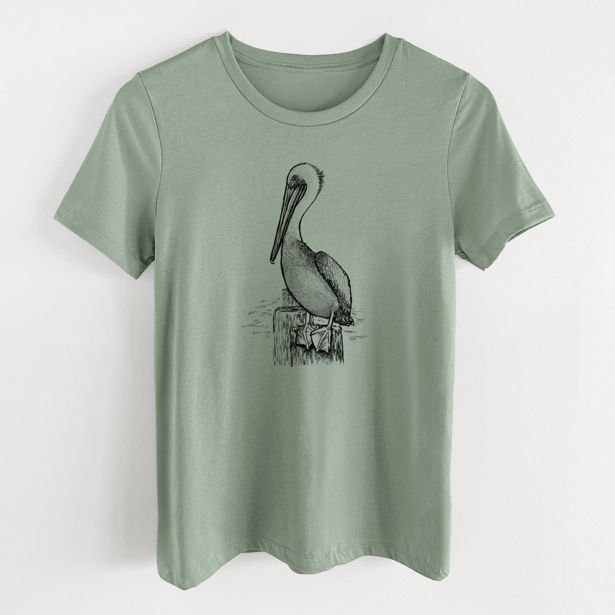 Sage green women's relaxed fit cotton t-shirt laid flat, printed with a detailed black ink illustration of a brown pelican perched on a wooden piling.