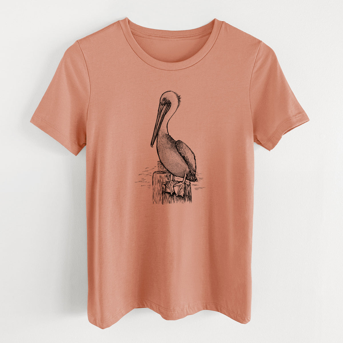 Terracotta orange women's relaxed fit cotton t-shirt laid flat, printed with a detailed black ink illustration of a brown pelican perched on a wooden piling.