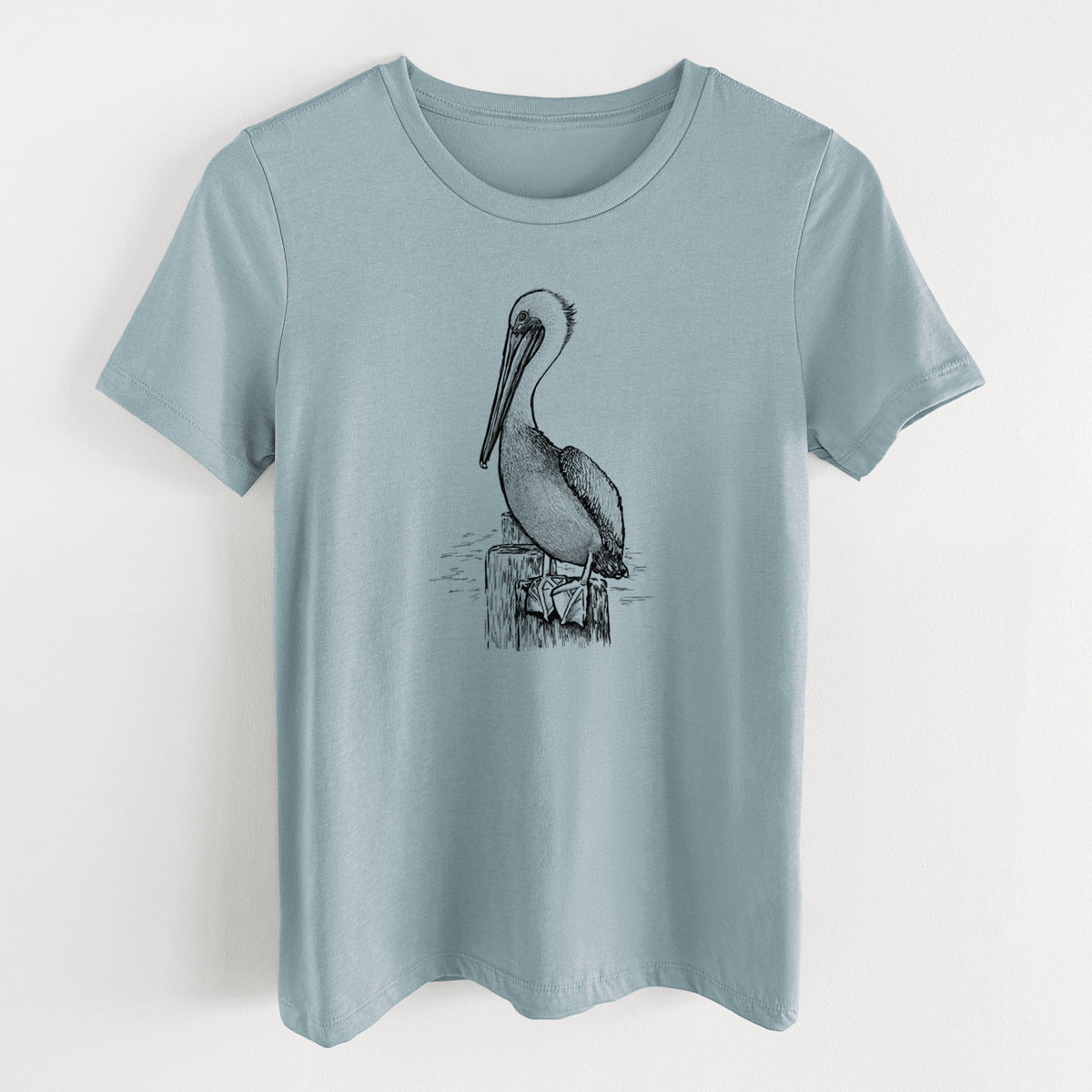 Vintage denim women's relaxed fit cotton t-shirt laid flat, printed with a detailed black ink illustration of a brown pelican perched on a wooden piling.