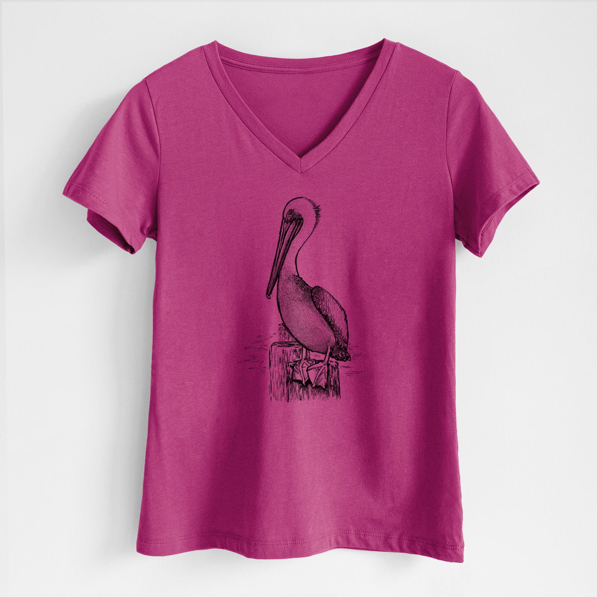 Berry pink women's relaxed fit cotton V-neck t-shirt laid flat, printed with a detailed black ink illustration of a brown pelican perched on a wooden piling.