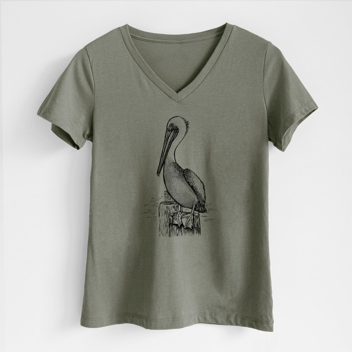 Military green women's relaxed fit cotton V-neck t-shirt laid flat, printed with a detailed black ink illustration of a brown pelican perched on a wooden piling.