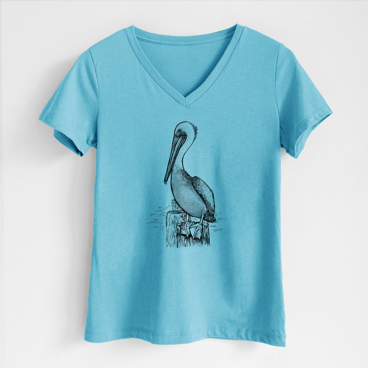 Turquoise women's relaxed fit cotton V-neck t-shirt laid flat, printed with a detailed black ink illustration of a brown pelican perched on a wooden piling.
