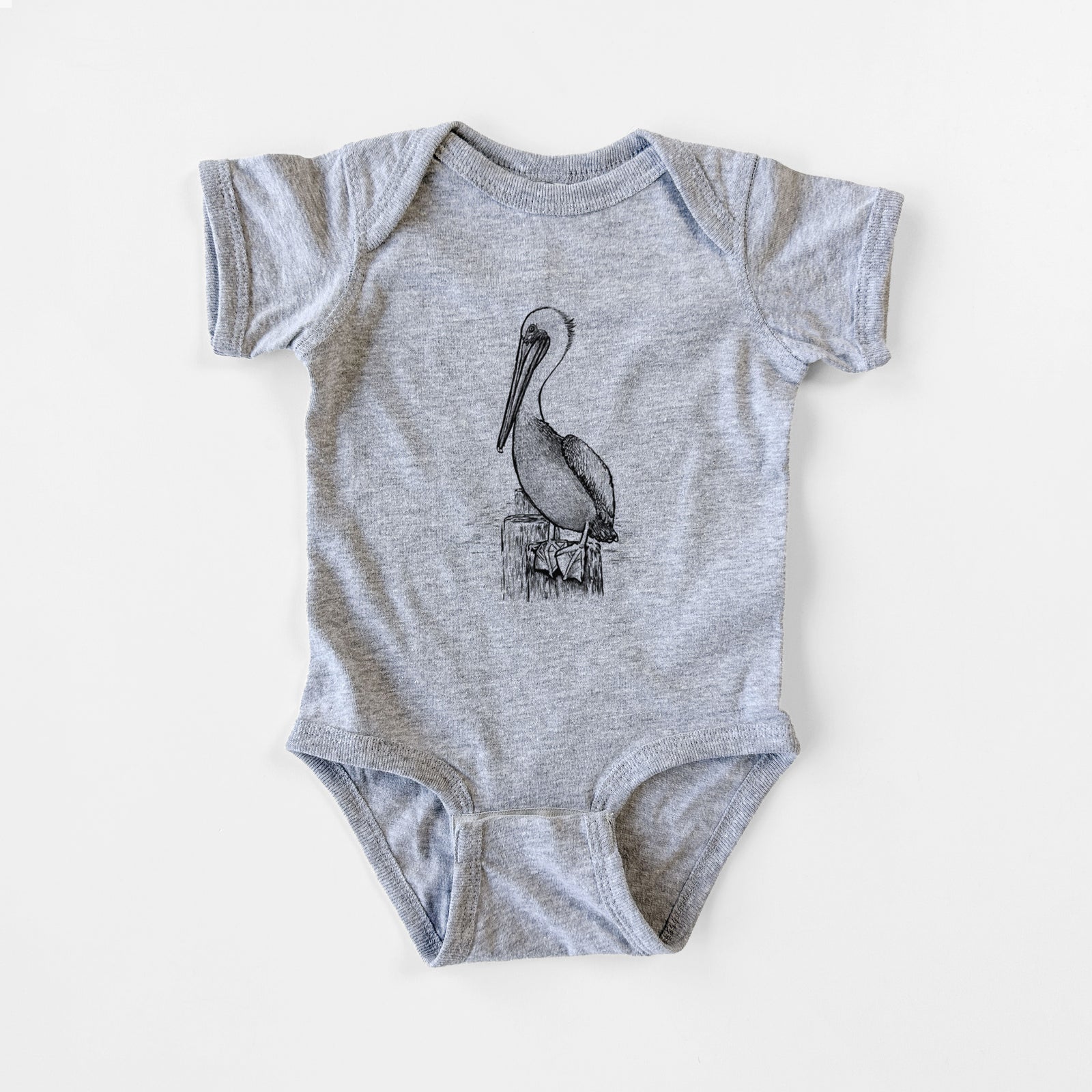 Grey baby bodysuit laid flat, printed with a detailed black ink illustration of a brown pelican perched on a wooden piling.