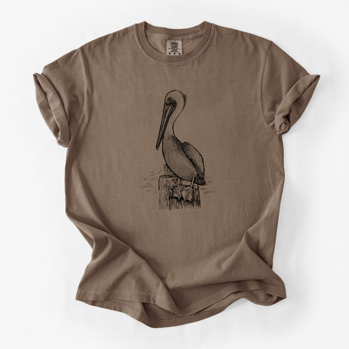 Espresso brown Comfort Colors t-shirt laid flat, printed with a detailed black ink illustration of a brown pelican perched on a wooden piling.