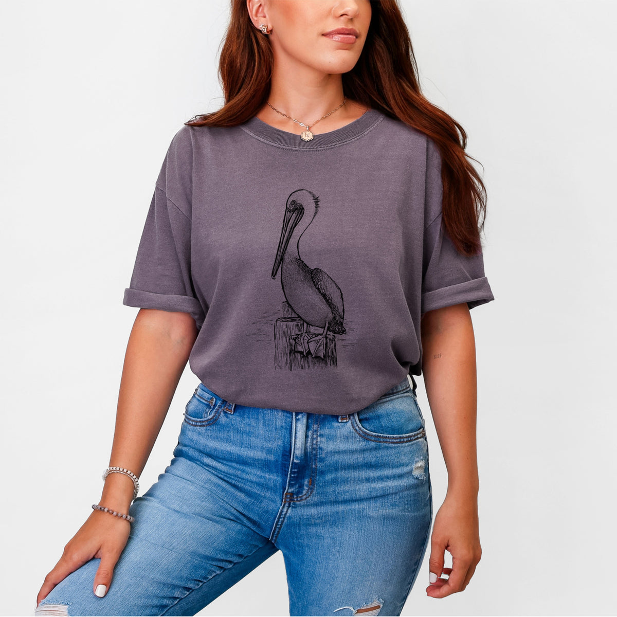 Woman wearing a Comfort Colors t-shirt printed with a detailed black ink illustration of a brown pelican perched on a wooden piling.