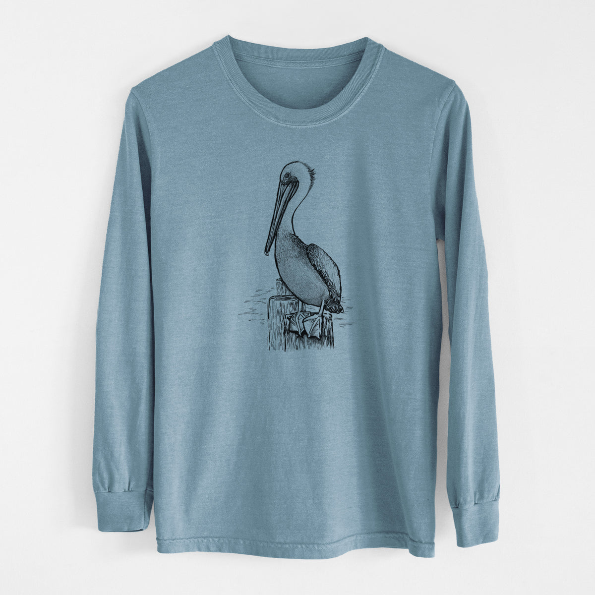 Steel blue Comfort Colors long sleeve shirt laid flat, printed with a detailed black ink illustration of a brown pelican perched on a wooden piling.