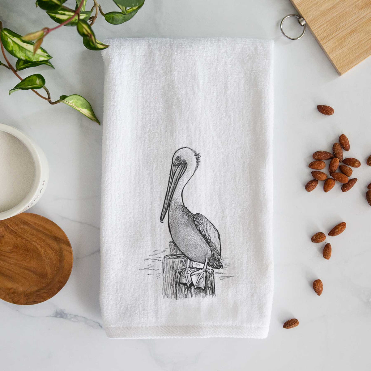 White hand towel printed with a detailed black ink illustration of a brown pelican perched on a wooden piling.
