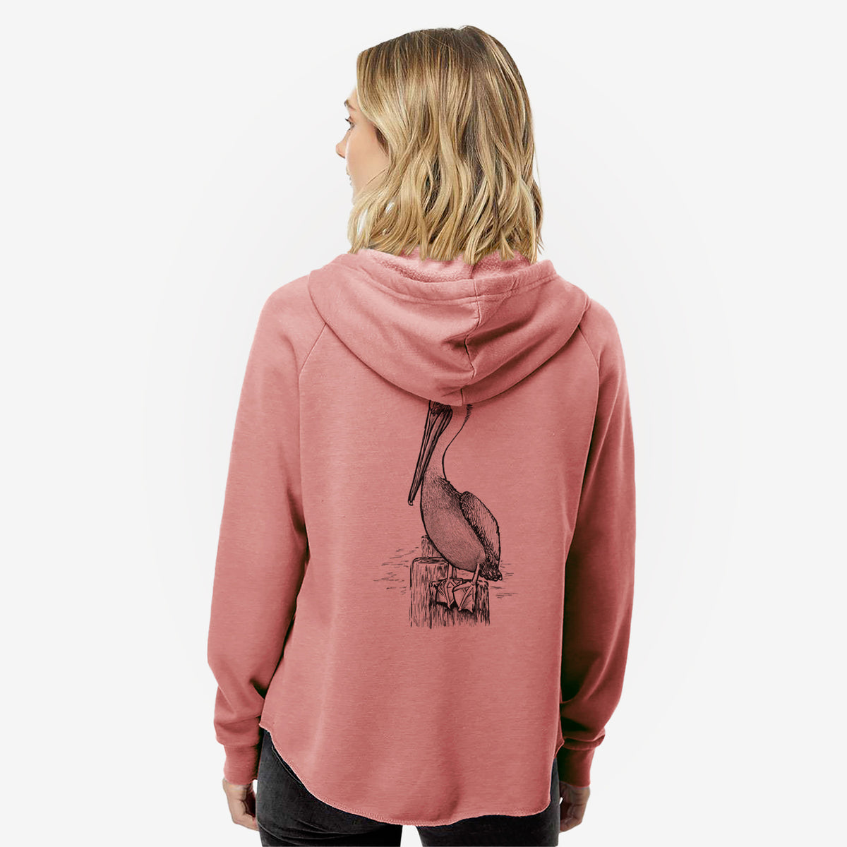 Woman wearing a dusty rose women's Cali Wave zip-up sweatshirt printed with a detailed black ink illustration of a brown pelican perched on a wooden piling, seen from behind.