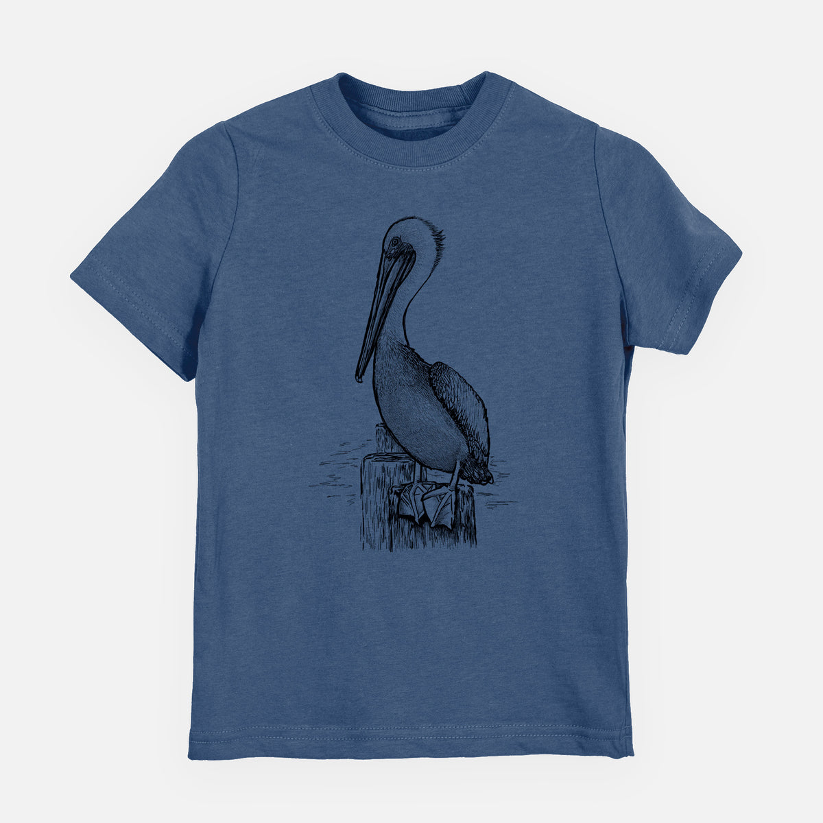 Indigo blue youth t-shirt laid flat, printed with a detailed black ink illustration of a brown pelican perched on a wooden piling.